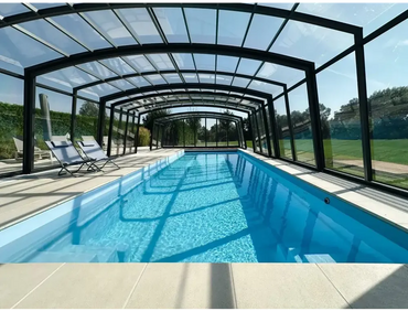 Lång rektangulär inomhuspool med klar blåvatten och svartramat glastak för Bahama trädgårdspool med transparent pooltak