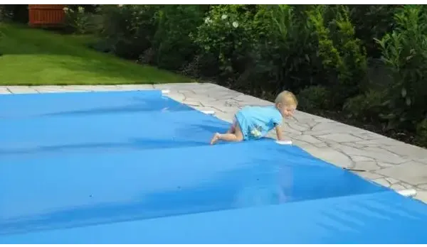 Barn i blå baddräkt kryper vid pool inkl handenhet med blå överdrag