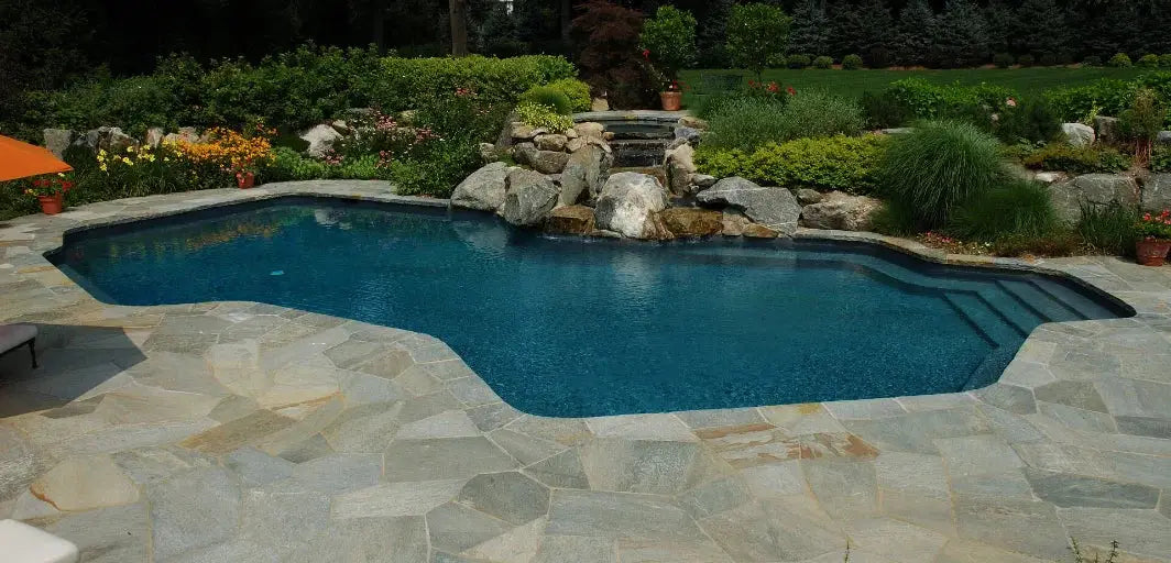 Lugn, oregelbunden inglaserad pool med blåvatten och stenplattor runt, varm under kalla månader.