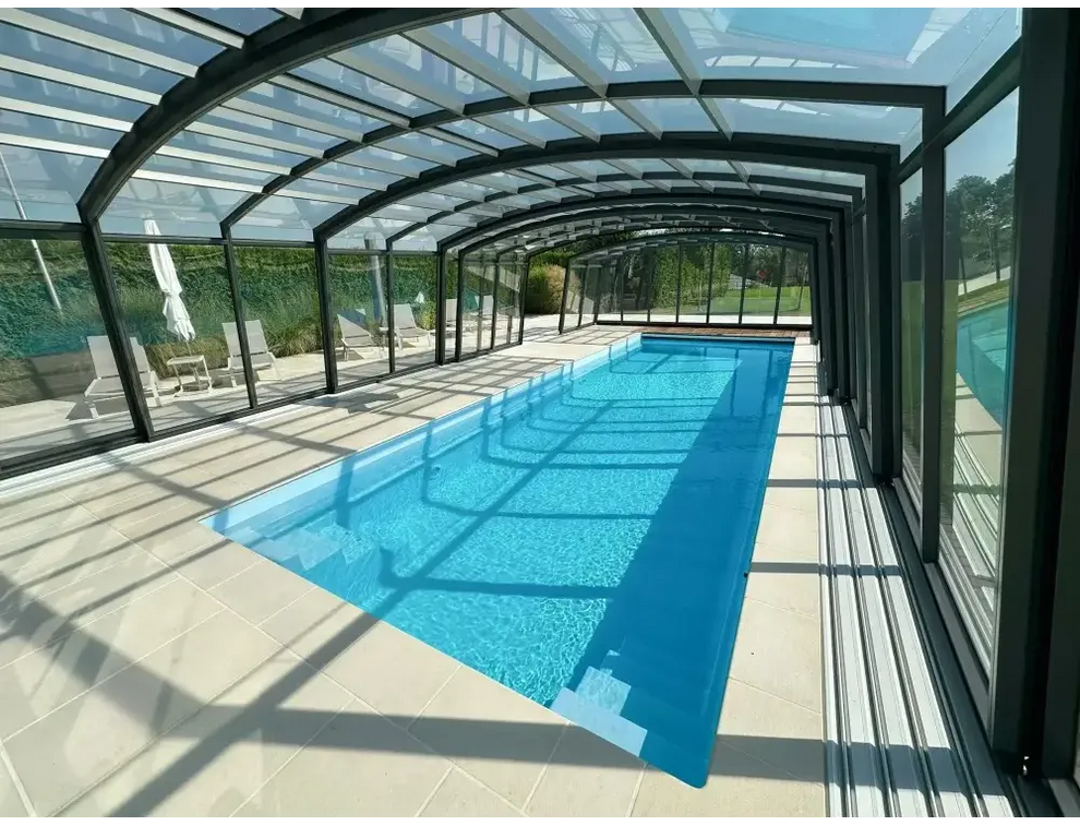 Lång rektangulär glasfiberpool Bahama med klart blått vatten, transparent glastak och svart metallram