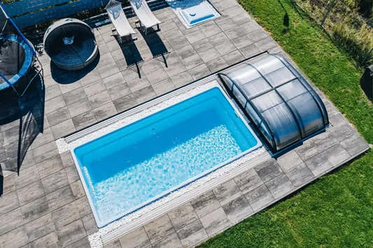 Glasfiberpool Papeete med klart blått vatten och transparent lock på grå stenplattor Glasfiberpool Papeete med klart blått vatten och transparent lock på grå stenplattor