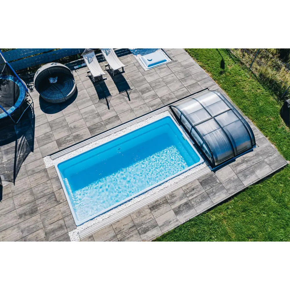 Rektangulär Glasfiberpool Papeete 700 med klart blått vatten och transparent pooltak på grå stenplattor