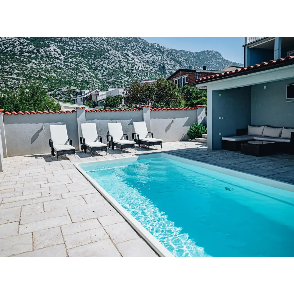 Glasfiberpool Saba 600 med klarblått vatten och vita kakelkanter