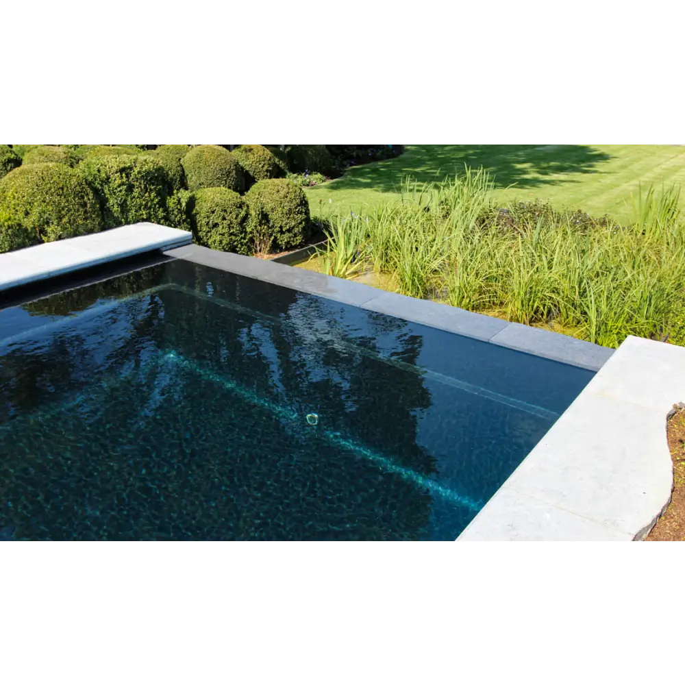 Rektangulär infinitypool Leisurepools Cube med mörkblått vatten och ljusa grå stenkanter