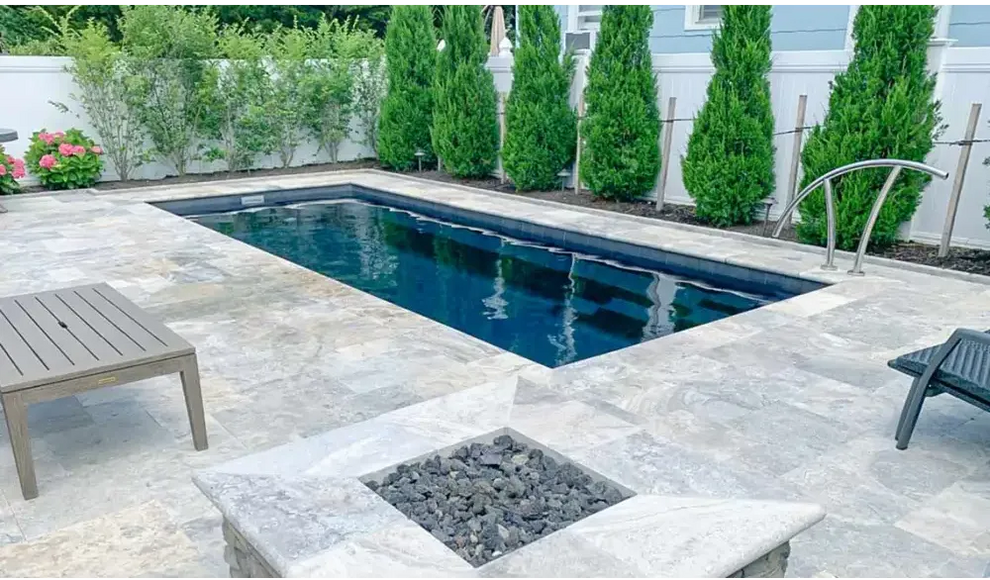 Rektangulär Leisurepools Harmony pool med klart blått vatten, grå sten och gröna träd