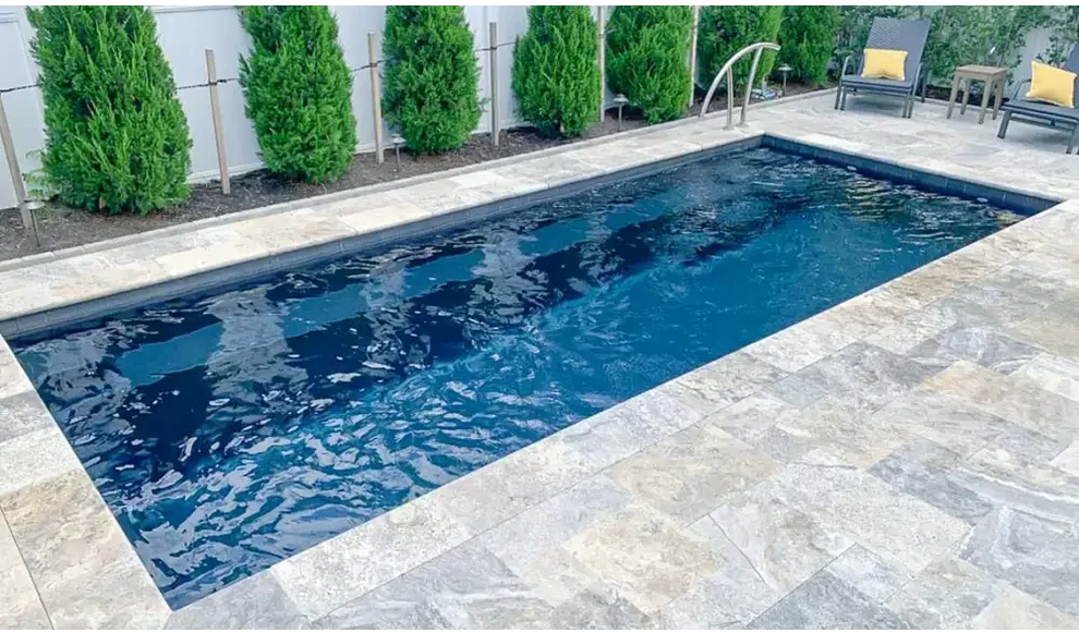 Rektangulär Leisurepools Harmony pool med klart blått vatten, grå sten och buskar