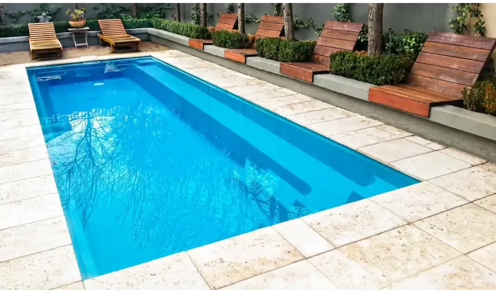 Rektangulär Leisurepools Harmony pool med klart blått vatten, stenplattor och trädeck