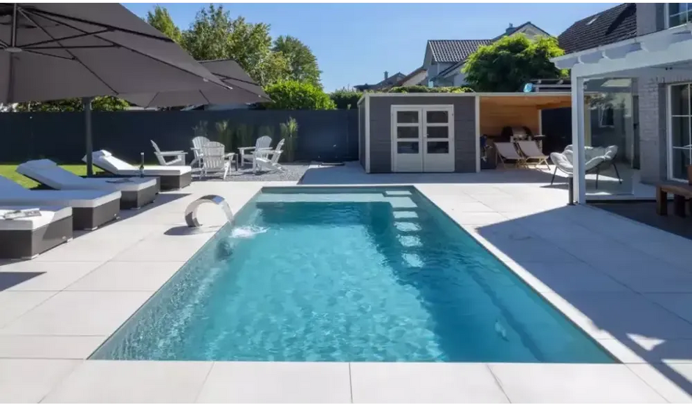 Rektangulär pool med kristallklart blått vatten, modern design, integrerad metallstege och visuellt imponerande hög vattenlinje