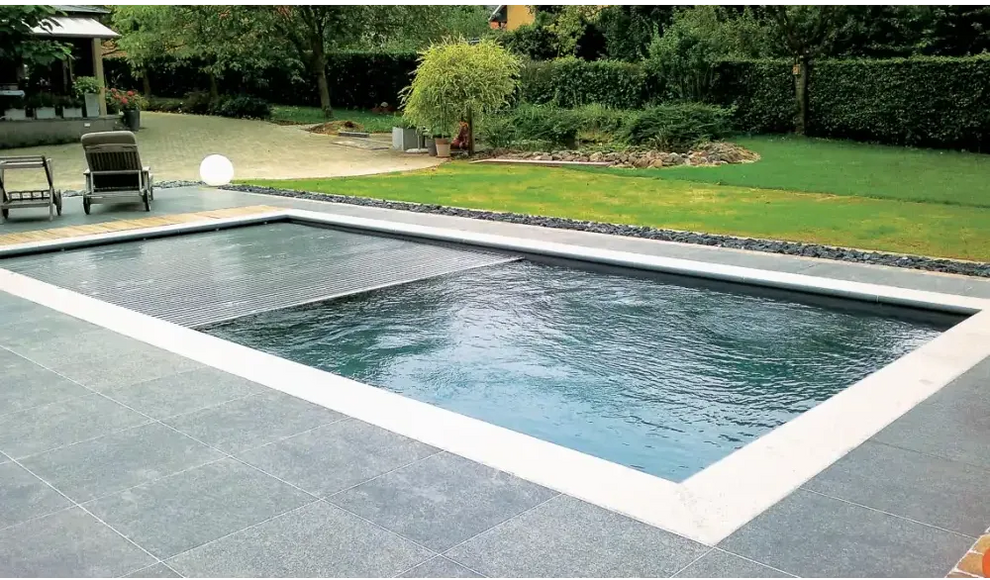 Leisurepools Reflection rektangulär ingroundbassäng med mörkblått vatten och vit kakelkant