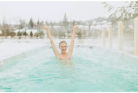Kvinna i rosa bikinitopp ler med armarna upp i PassionSpa Activity 2 Swim Spa omgiven av snö