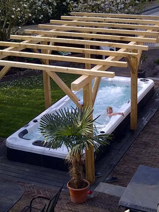 Vit och svart PassionSpa Aquatic 2 Swim Spa med bubblande vatten under pergola Vit och svart PassionSpa Aquatic 2 Swim Spa med bubblande vatten under pergola
