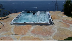 Grå PassionSpa Euphoria Mighty Wave Spabad med svarta jetstrålar på stenaltan vid havet