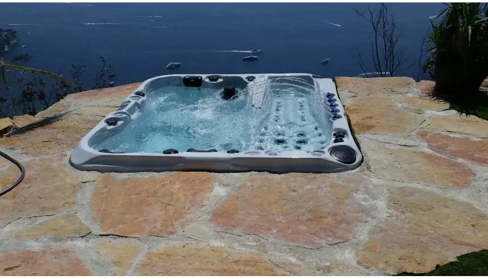 Grå PassionSpa Euphoria Mighty Wave Spabad med svarta jetstrålar på stenaltan vid havet