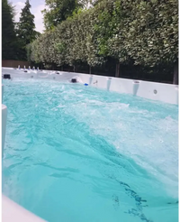 Vit PassionSpa Spirit Deep Swim Spa med turkost vatten och jetstrålar omgiven av gröna träd