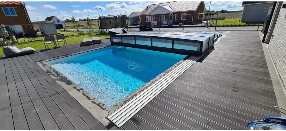 Rektangulär pool med klart blått vatten, grå trädeck och modernt glastak i Pooltak Icon Kit