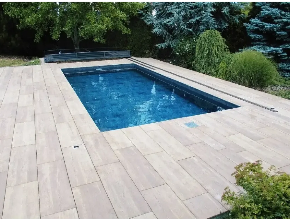 Rektangulärt Pooltak Mästare Plus med klarblått vatten, grå stenplattor och gröna träd