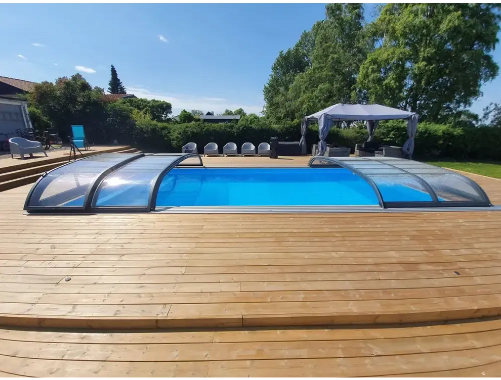 Blå pool med genomskinlig bågad pooltäckning i Pooltak Nivo Kit 1060B på trädeck