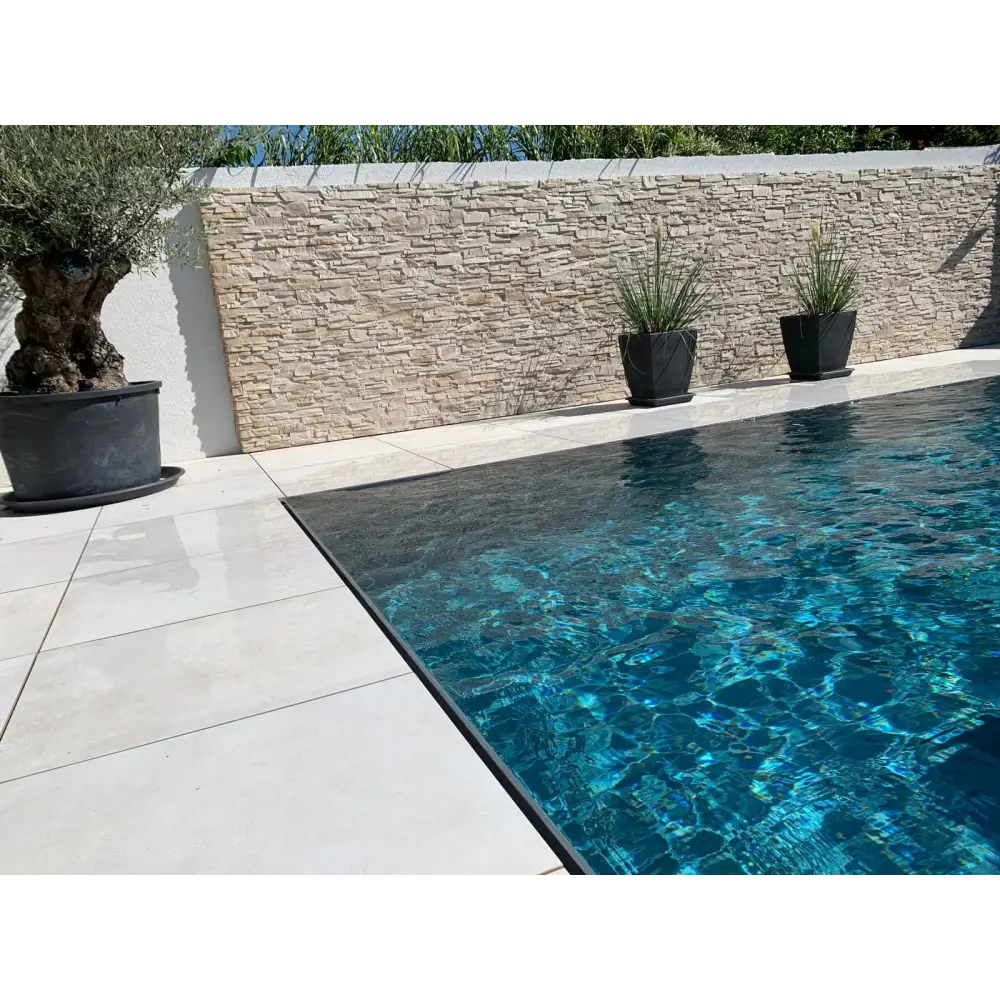 Kristallklar turkos pool med svarta kakelkanter och stenbakgrund i Pooltime Exclusive overflow PP pool