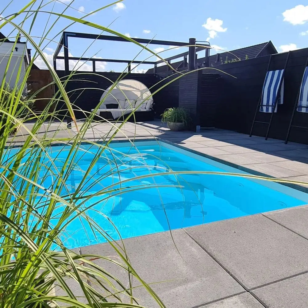 Pooltime Exklusiv vid kristallklar blå pool med kakelkanter och grönska