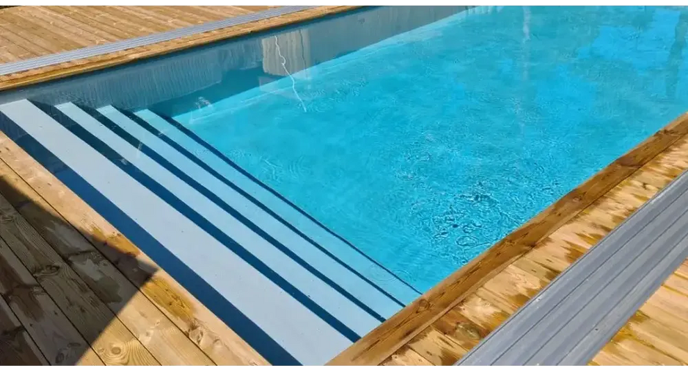 Pooltime Exklusiv 12mm rektangulär pool med klart blått vatten, trädeck och grå metalltrappor
