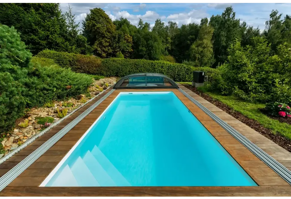 Rektangulär Thermopp Poolpaket Qbig med klart blått vatten, trädeck och grönska