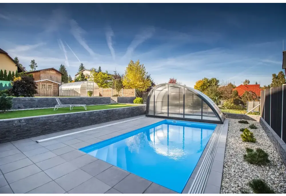 Blå rektangulär pool med genomskinlig valv och grå stenplattor i Thermopp Poolpaket Qbig