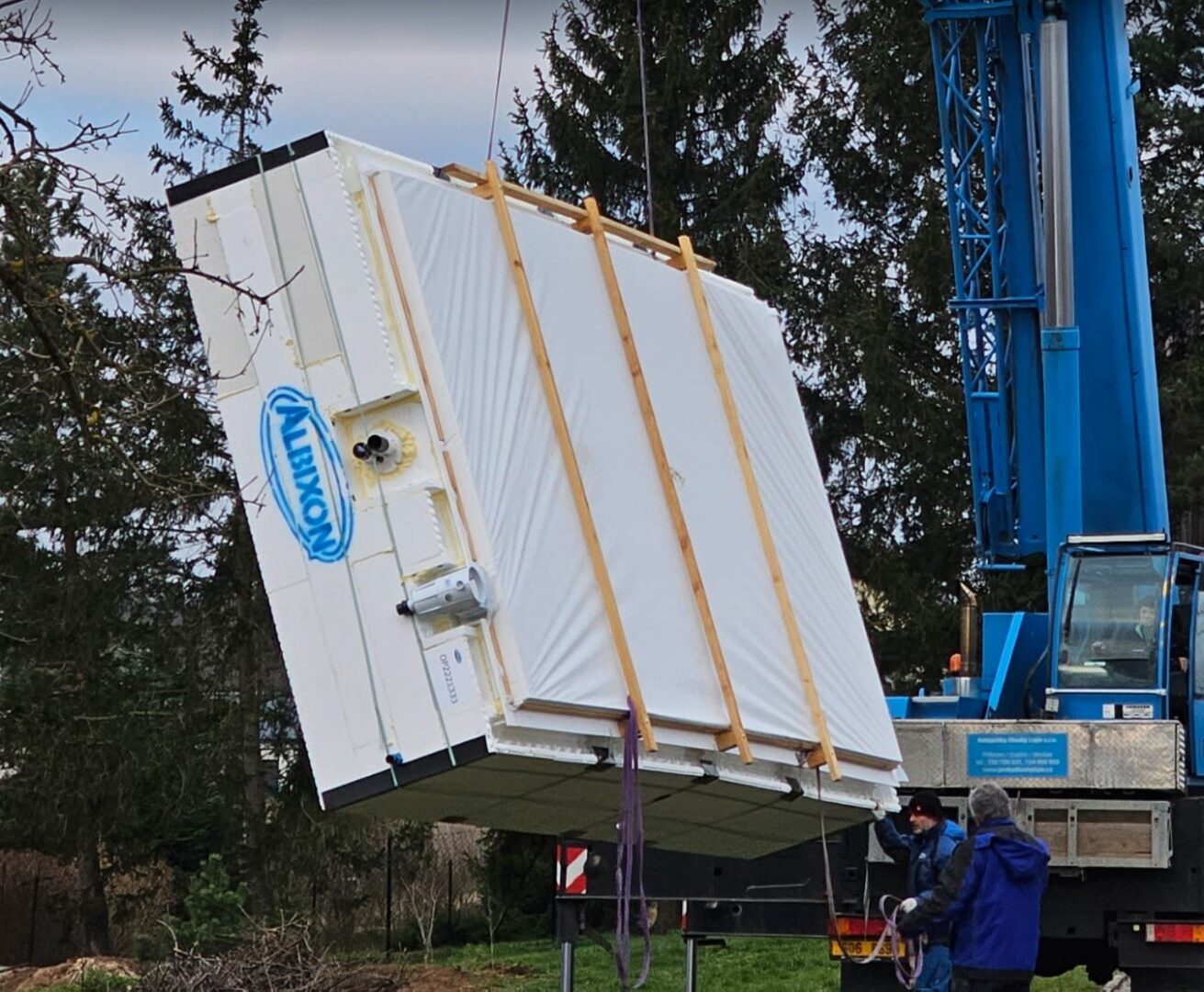 En kran lyfter utan ansträngning en stor vit container märkt MOMINIT utomhus.